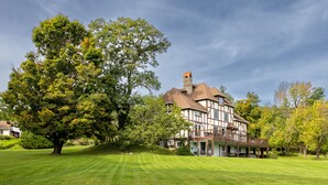 A large, two-story house with a prominent chimney, surrounded by a well-maintained lawn and mature trees. - Rent an entire lake-view estate in the heart of wine country!   (Hammondsport)