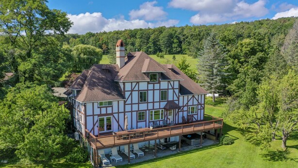 A large, two-story house with a balcony and a deck, surrounded by lush greenery and trees. - Rent an entire lake-view estate in the heart of wine country!   (Hammondsport)