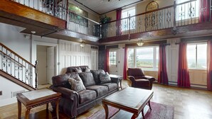 A spacious living room with a leather sofa, a wooden coffee table, and a high wooden staircase with wrought iron railings. - Rent an entire lake-view estate in the heart of wine country!   (Hammondsport)