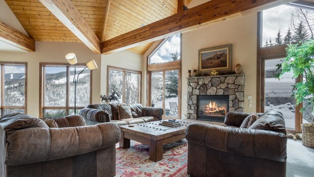 A cozy living room with leather sofas, a stone fireplace, and large windows offering a view of snowy mountains. - Panoramic View, Great Outdoor Space, Private Elevator, Monthly Rentals Available (Vail)