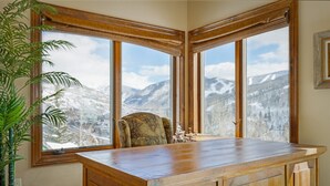 A corner room with a wooden desk and a chair, large windows with a mountain view, and a potted plant. - Panoramic View, Great Outdoor Space, Private Elevator, Monthly Rentals Available (Vail)