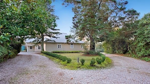 Uma casa com entrada por caminho de pedras, gramado bem cuidado e diversas árvores.