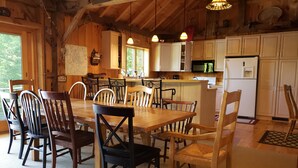 A wooden lodge dining area with a large table and chairs, a kitchen with white cabinets, and a view of the outdoors. - Stunning view from this secluded mountain gettaway (West Alton)