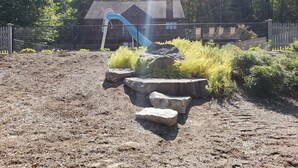 A playground with a slide, surrounded by rocks and plants, and a building with a chimney in the background. - Stunning view from this secluded mountain gettaway (West Alton)