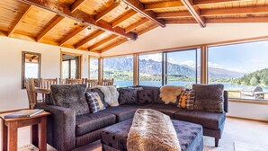 Ein modernes Wohnzimmer mit einer großen Eckcouch, einem Holztisch und Blick auf Berge und einen See.