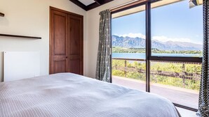 Ein Schlafzimmer mit einem großen Bett, einer Holztür und Blick auf Berge und einen See durch ein großes Fenster.