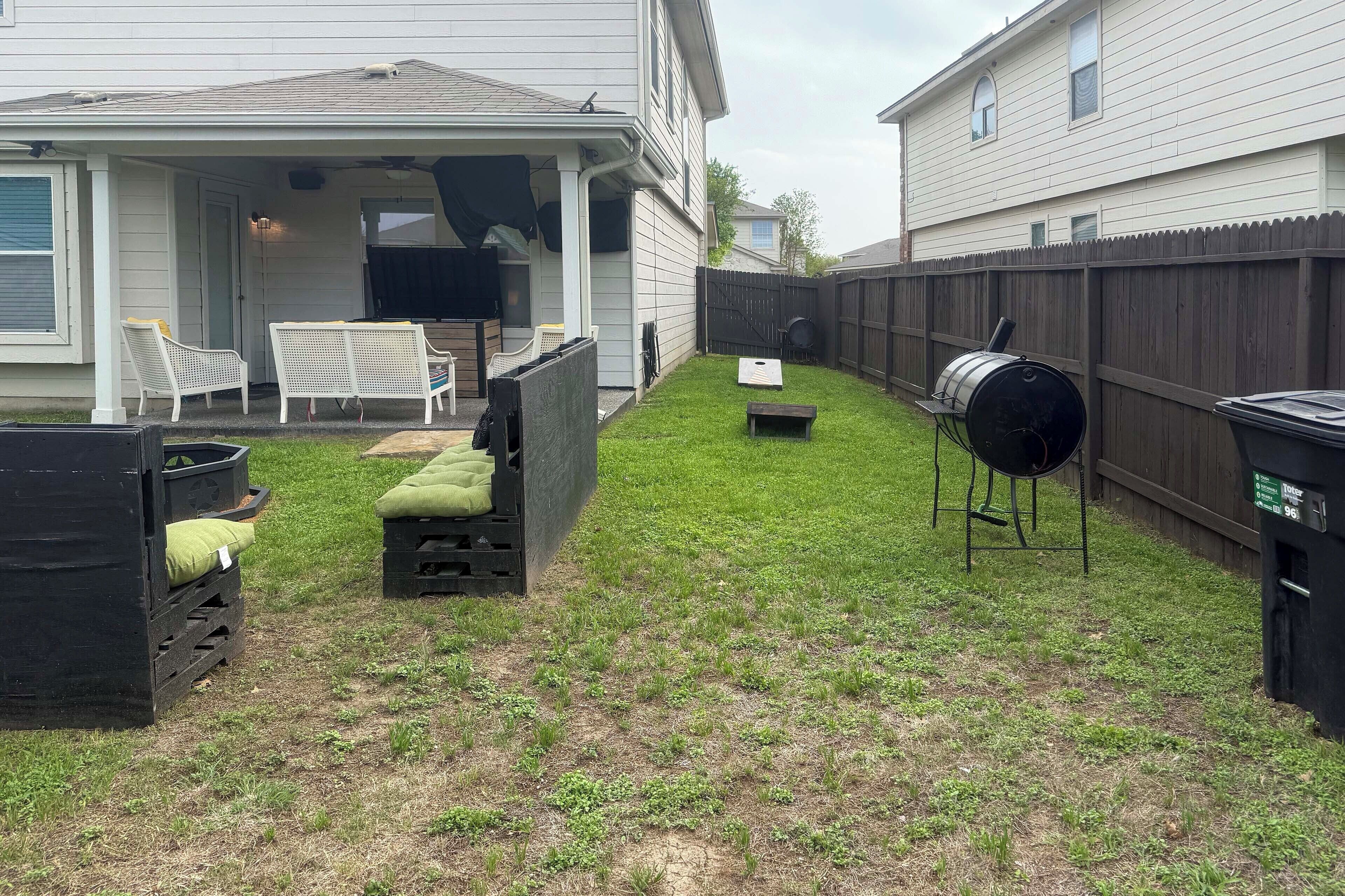 A backyard with a covered patio, outdoor furniture, a barbecue grill, and a fenced area.