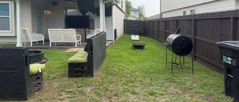 A backyard with a covered patio, outdoor furniture, a barbecue grill, and a fenced area.