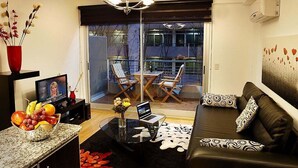 A modern living room with a black leather sofa, a glass coffee table, a laptop, and a dining area with a table and chairs.