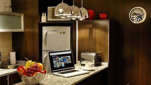 A modern kitchen with a laptop, a bowl of fruit, a toaster, and a clock on the wall.