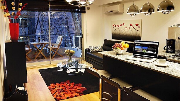 A modern kitchen with a laptop, a coffee maker, and a dining area with a glass table and chairs.