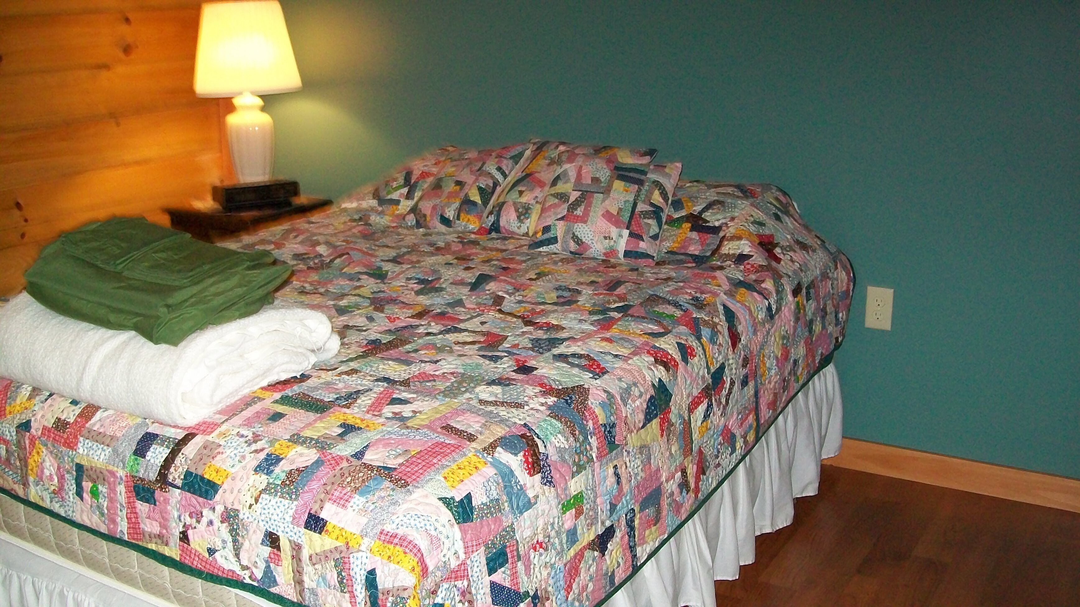 Ein Bett mit einer farbenfrohen Steudecke, einer grünen Decke und einem weißen Handtuch.