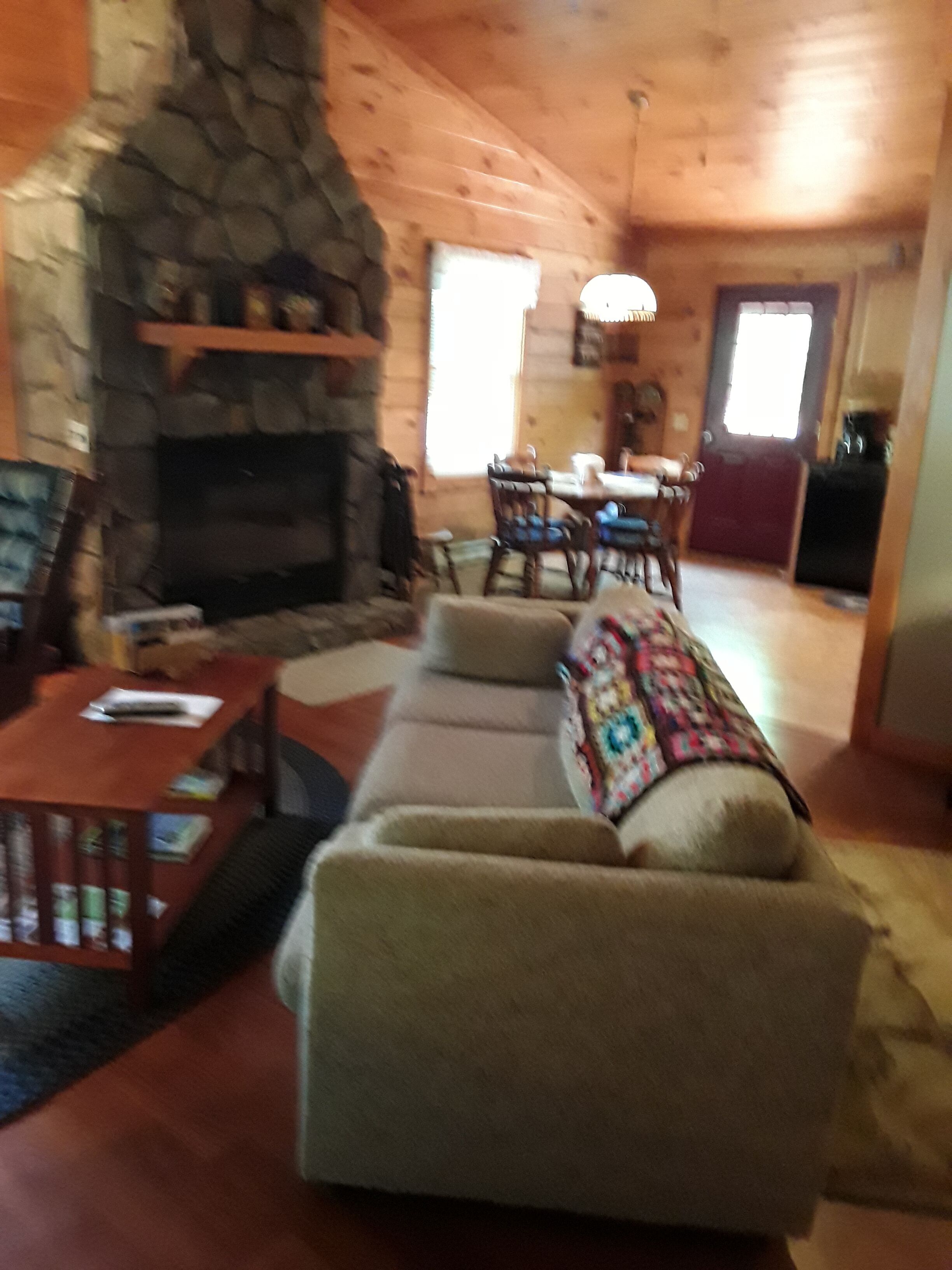 A cozy living room with a stone fireplace, a sofa, a coffee table, and a dining area with a table and chairs.