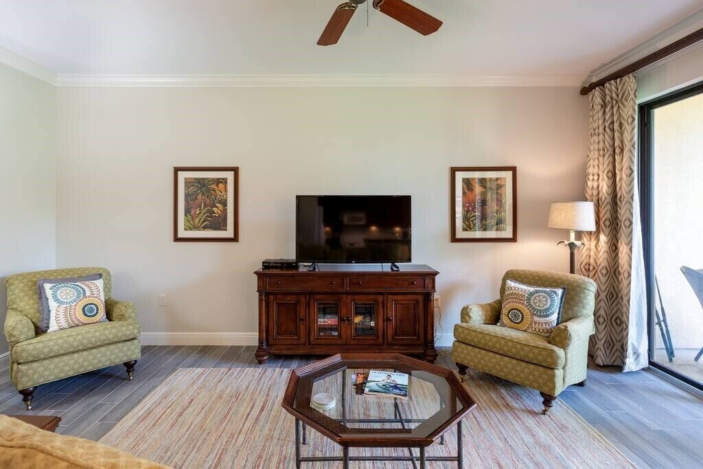 A living room with two armchairs, a coffee table, a TV on a wooden cabinet, and framed artwork on the walls.