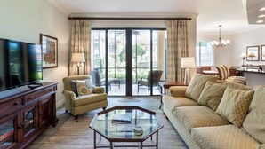 A living room with a sofa, armchair, coffee table, TV, and a view through a glass door to an outdoor area. - Bay Bungalow at Naples Bay Resort (Naples)