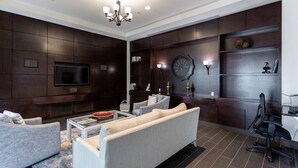 A modern living room with a large flat-screen TV, a chandelier, dark wood paneling, a sofa, a coffee table, and a bookshelf. - Bay Bungalow at Naples Bay Resort (Naples)