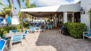 An outdoor patio with tables and chairs, palm trees, and a covered seating area. - Bay Bungalow at Naples Bay Resort (Naples)