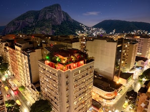 A high-rise building with multiple floors, balconies, and a rooftop terrace with plants.
