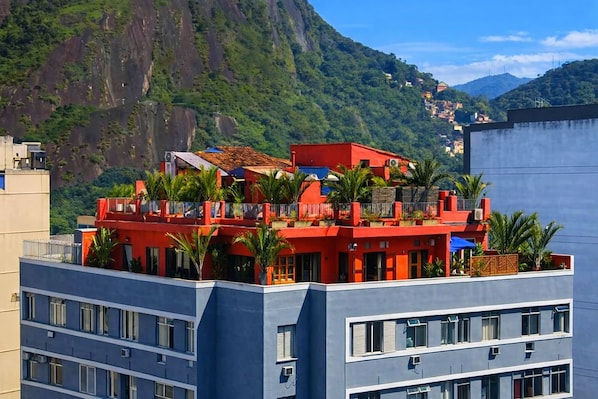 A multi-story building with balconies, surrounded by greenery and mountains.