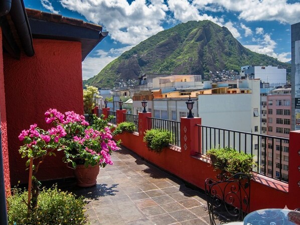 Un balcón con plantas en macetas, barandilla de metal y vista a la montaña.