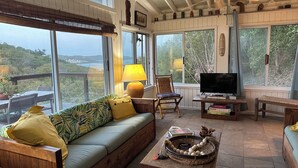 Ein gemütliches Wohnzimmer mit einer Couch, einem Fernseher und Blick ins Freie.