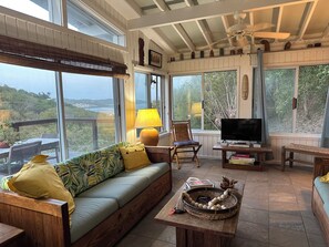 Ein gemütliches Wohnzimmer mit einer Couch, einem Fernseher und Blick ins Freie.