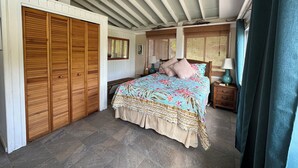 Ein Schlafzimmer mit Bett, Holzschrank, Deckenventilator und Fenster mit Vorhängen.