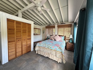 Ein Schlafzimmer mit Bett, Holzschrank, Deckenventilator und Fenster mit Vorhängen.