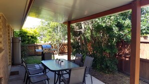 Une terrasse couverte avec une table et des chaises, un barbecue et un chauffe-eau.