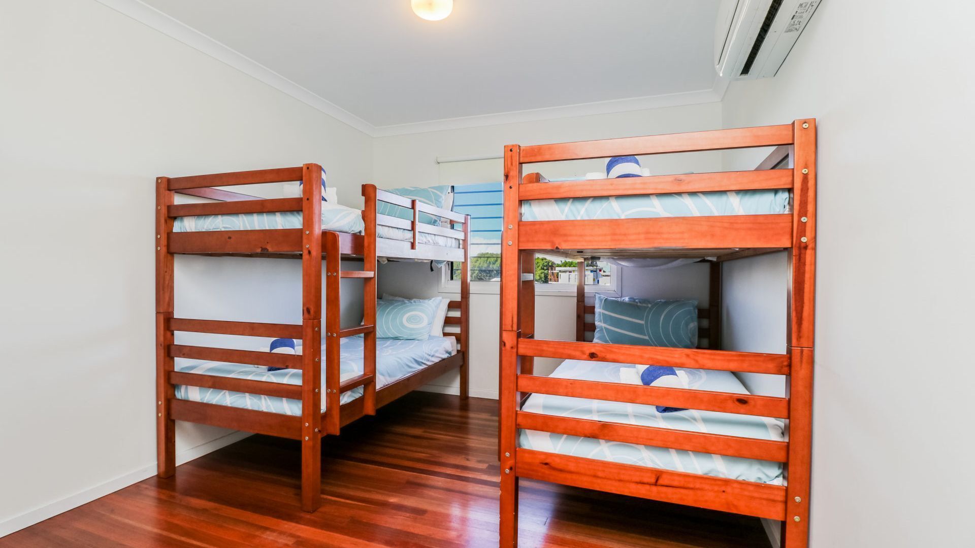 A room with two bunk beds, wooden flooring, and a window with a view of greenery.