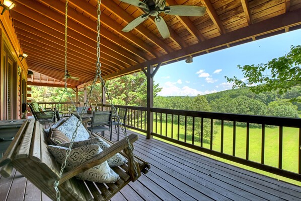 Une terrasse en bois avec un fauteuil suspendu, du mobilier d’extérieur et une vue sur un paysage verdoyant.