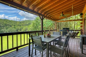 Une terrasse extérieure couverte, équipée d’une table et de chaises, d’un barbecue et offrant une vue sur une zone boisée.