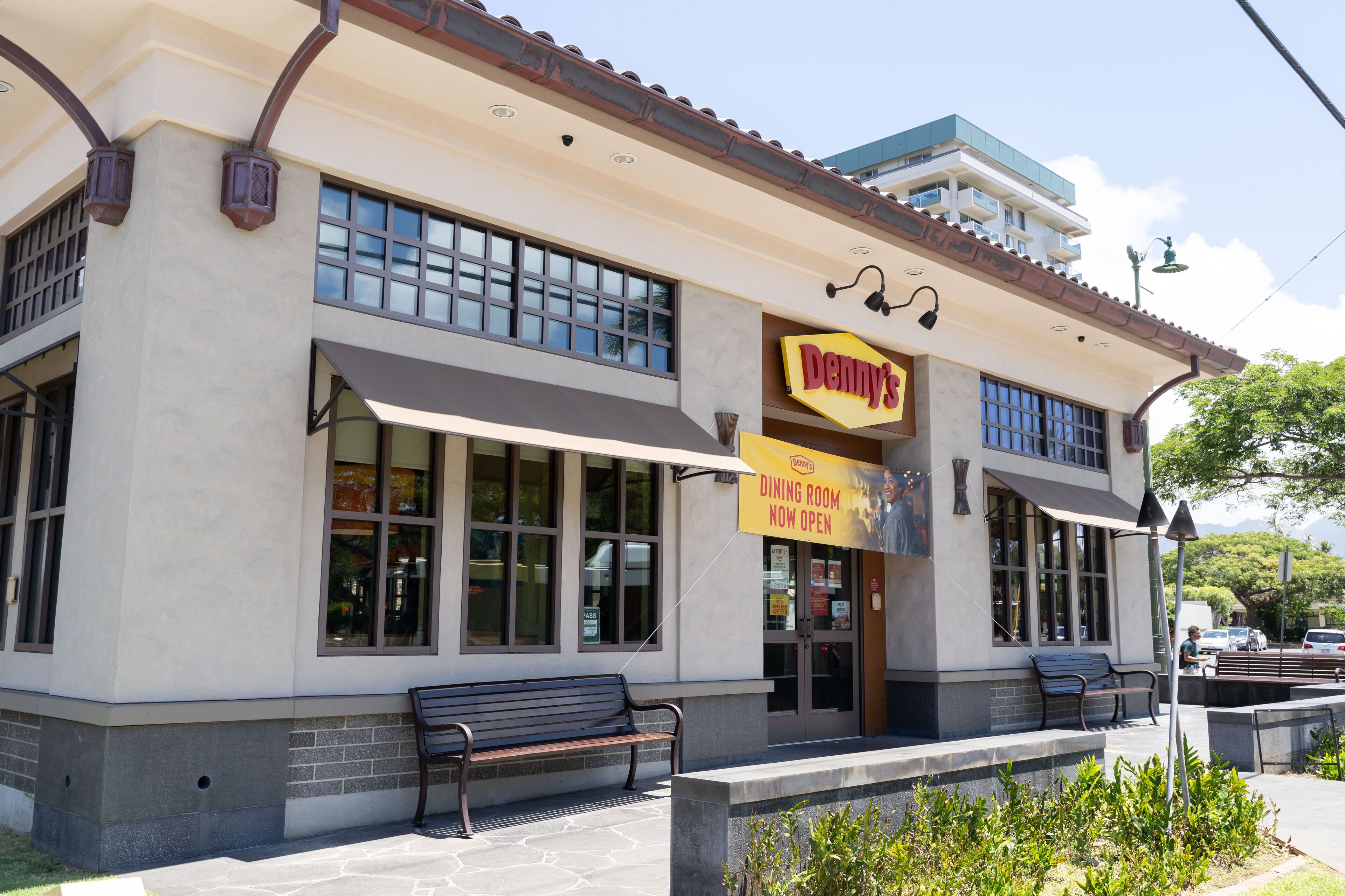Un bâtiment avec une enseigne « Denny's », des tables à l'extérieur et une pancarte indiquant « Salle à manger ouverte ».