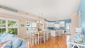 A spacious kitchen with white cabinets, a dining area with a wooden table and chairs, and a view of the outdoors through large windows. - Rare private beach side location that also has beautiful bayside views (Bethany Beach)