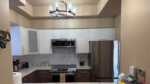 A modern kitchen with white cabinets, stainless steel appliances, a marble countertop, and a chandelier. - Ventana Canyon Resort-Style Condominium (Tucson)