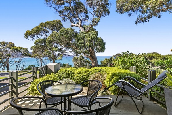 A patio with outdoor seating, a view of the sea, and a large tree.