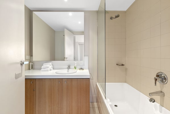 A modern bathroom with a glass shower enclosure, a white sink, and wooden cabinets. - Apartment 2 Kalimna (Lorne)