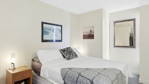 A hotel room with a bed, a nightstand, a bedside table, a mirror, and two framed pictures on the wall. - Apartment 2 Kalimna (Lorne)
