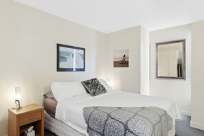 A hotel room with a bed, a nightstand, a bedside table, a mirror, and two framed pictures on the wall.
