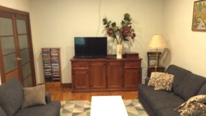 A living room with two sofas, a TV on a wooden cabinet, a lamp, and a vase with flowers. - The Grove Gunbower.. (Gunbower)