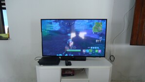 Uma televisão em cima de um armário branco, com controle remoto e decodificador.