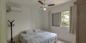 A bedroom with a bed, a ceiling fan, an air conditioning unit, a window with curtains, and a coat rack.