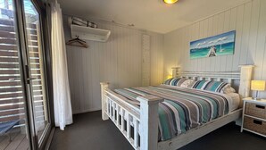 A bedroom with a bed, a nightstand, a lamp, a painting, a window with blinds, and a hanging coat rack. - Pet-Friendly | 200m to Beach | Sleeps Large Groups | Beach Views | Air Con (Callala Beach)