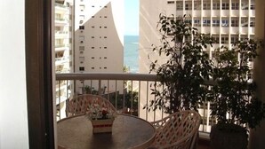 A balcony with a table and chairs, overlooking a cityscape and the sea. - Mi's Apartment - 2 minutes from Pitangueiras Beach - Guarujá (Guarujá)