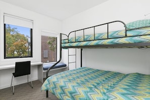 A bunk bed with a patterned bedspread, a desk with a chair, and a window with a view of trees.