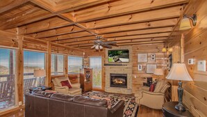 A cozy cabin interior with a fireplace, wooden walls, a leather sofa, and a ceiling fan. - 🏔️ A Starr Peak View🌲 Resort Pool, Hot Tub & Game Room (Sevierville)