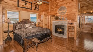 A log cabin bedroom with a bed, two lamps, a fireplace, and a ceiling fan. - 🏔️ A Starr Peak View🌲 Resort Pool, Hot Tub & Game Room (Sevierville)