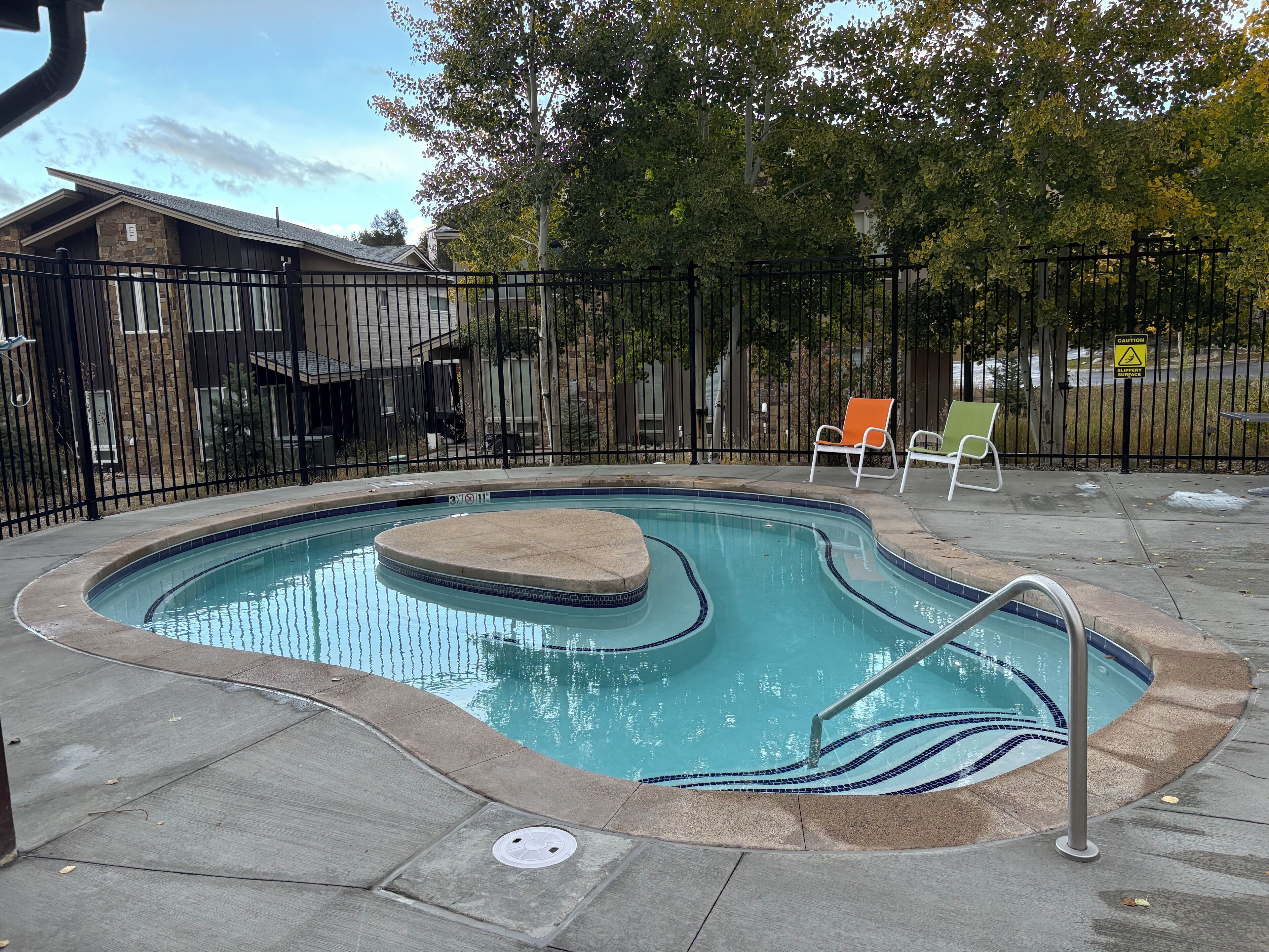 Una piscina con cubierta de piedra, escalera metálica y dos sillas reclinables.