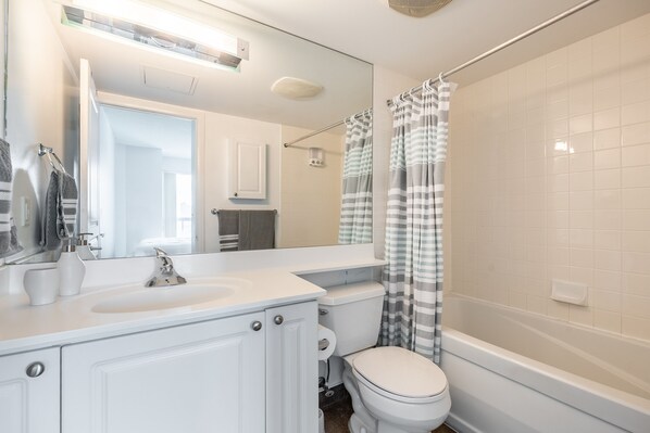 Une salle de bain moderne avec un lavabo blanc, un miroir et des toilettes. On y trouve un rideau de douche et une baignoire.