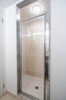 Een douche met glazen wanden, bekleed met beige tegels en een metalen frame.
